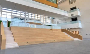 The interior atrium showing the social staircase from the front. Staircase is made of lightly colored wood.